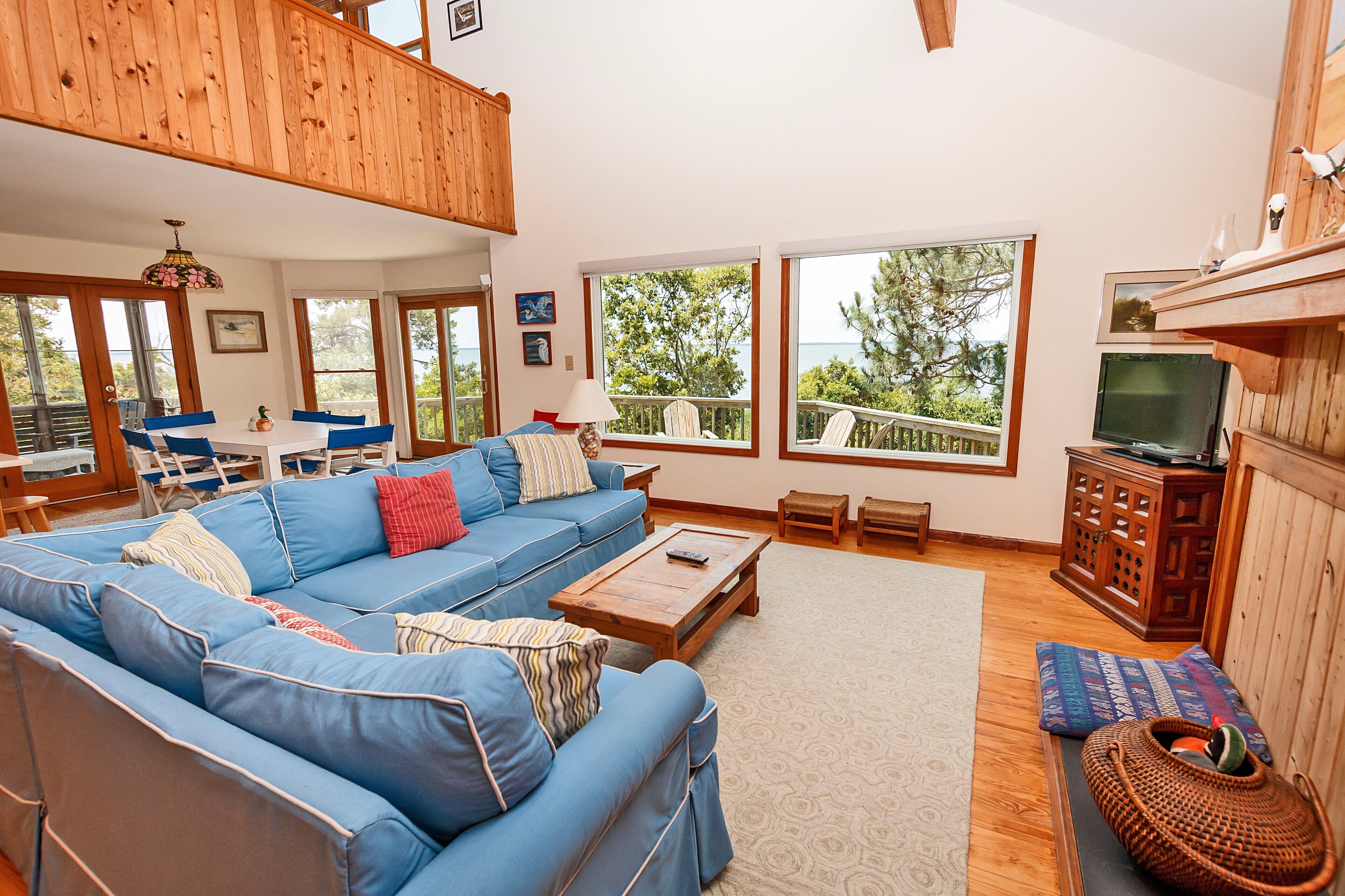 A spacious living room with a high ceiling, a blue sofa set, a wooden coffee table, and a television on a wooden cabinet.