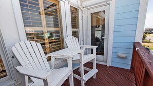 A wooden deck with two white Adirondack chairs and a small table.