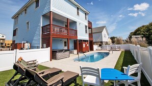 A two-story house with a swimming pool, outdoor furniture, and a fenced yard.