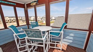 A covered outdoor area with a white table and chairs, large windows, and a view of a residential area.