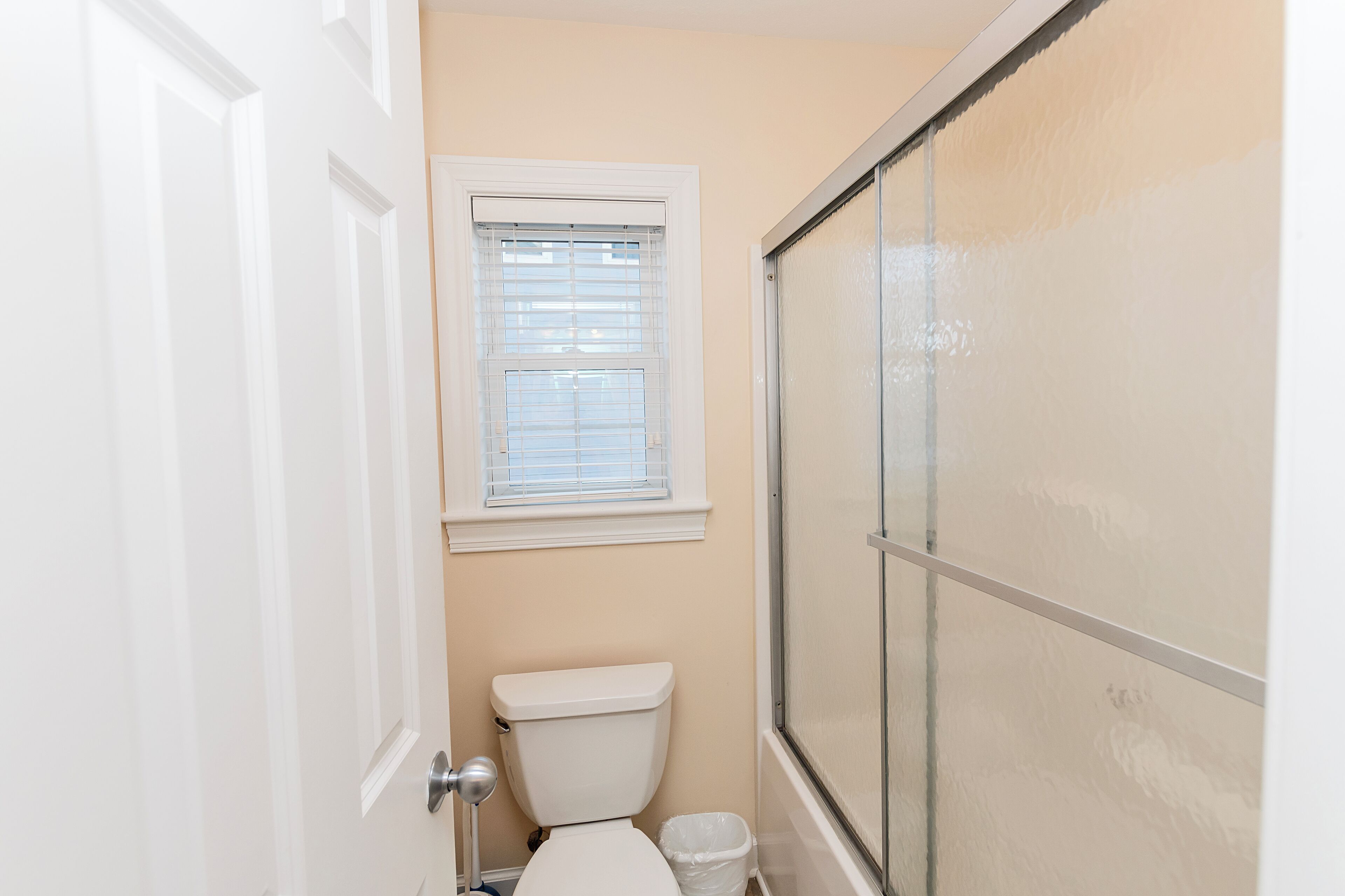 A small bathroom with a toilet, a window, and a shower enclosure.