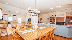 A spacious kitchen with wooden chairs, a dining table, and a chandelier. There is a living area with a sofa and a fireplace. - Oceanside, Private Pool, Community Amenities, Hot Tub, VOH94, Knot A Problem (Corolla)