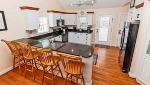 A kitchen with a central island, wooden chairs, white cabinets, and a black refrigerator. - Oceanside, Private Pool, Community Amenities, Hot Tub, VOH94, Knot A Problem (Corolla)