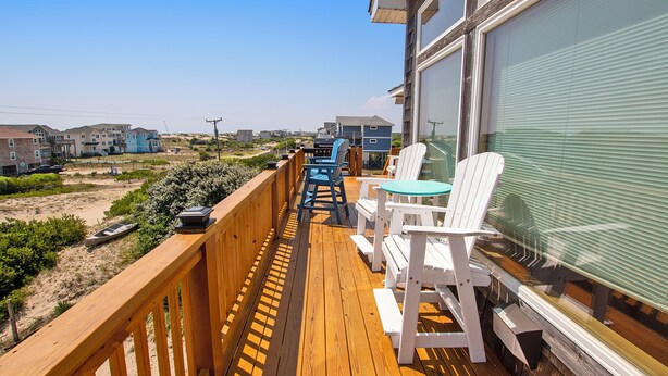 Un pontile in legno con mobili da esterno, vista su una zona residenziale con case e una spiaggia.