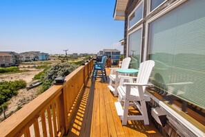 A wooden deck with outdoor furniture, overlooking a residential area with houses and a beach.