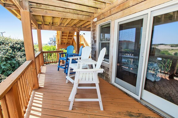 Una terraza de madera con una mesa, sillas, un ventanal corredero y vista a la playa.