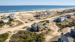 An aerial view of a coastal residential area with houses, a beach, and a clear sky.