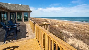 A wooden deck with blue Adirondack chairs, a glass door, and a view of the beach. - OCEANFRONT, Ocean Views, Sun Decks, Close to Beach Access, SA112, The SandBar (Duck)