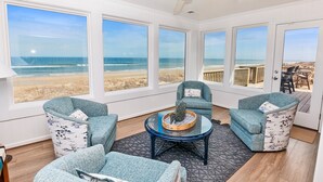 A room with large windows overlooking a beach, furnished with blue chairs and a coffee table. - OCEANFRONT, Ocean Views, Sun Decks, Close to Beach Access, SA112, The SandBar (Duck)
