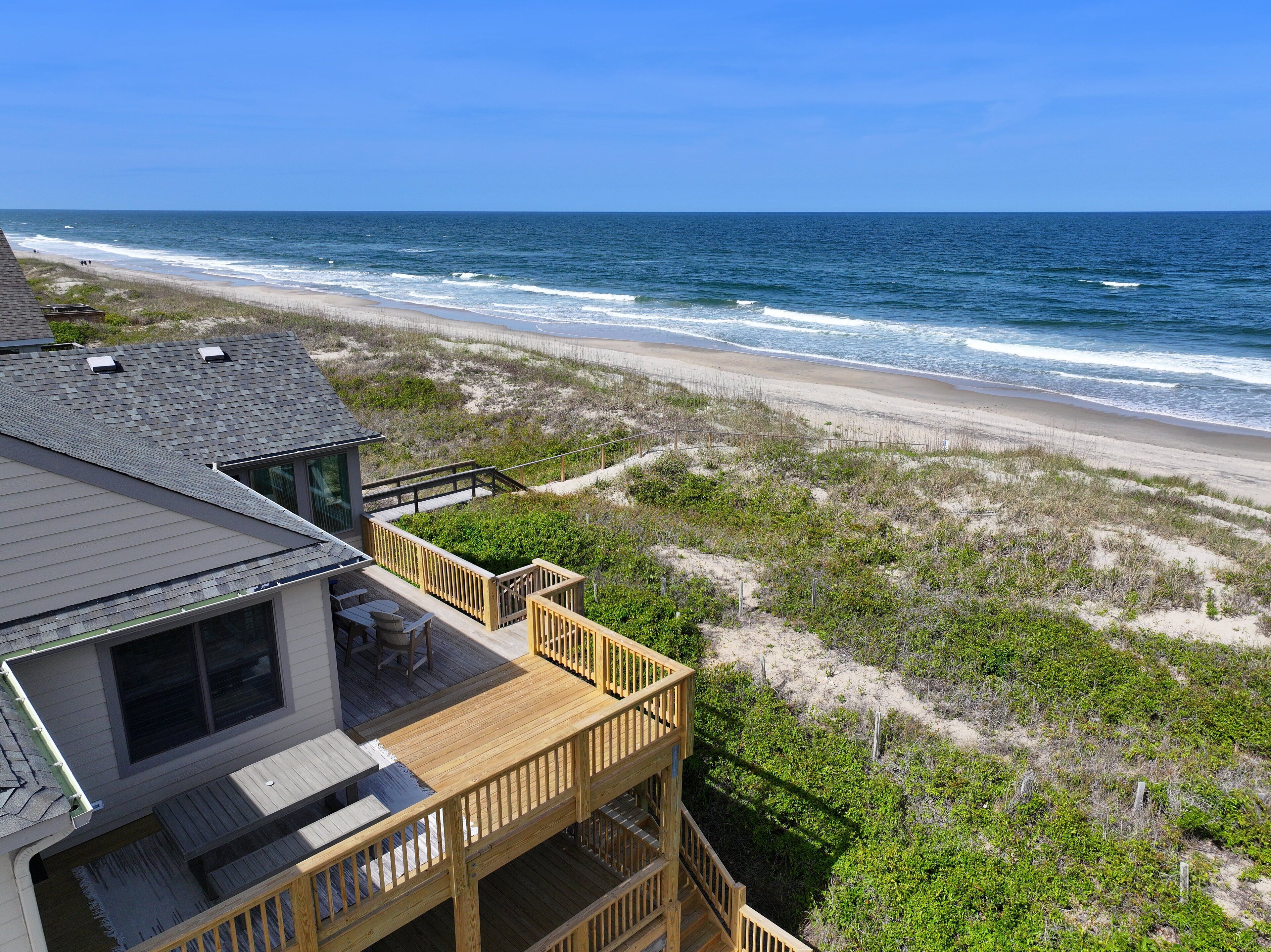 A beachfront property with a wooden deck, a view of the ocean, and a sandy beach.