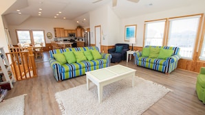 A spacious living area with striped sofas, a coffee table, and a dining area with wooden furniture. - Oceanside, Heated Pool, Poolside Pavilion, Hot Tub, 4, Relax Mom (Corolla)
