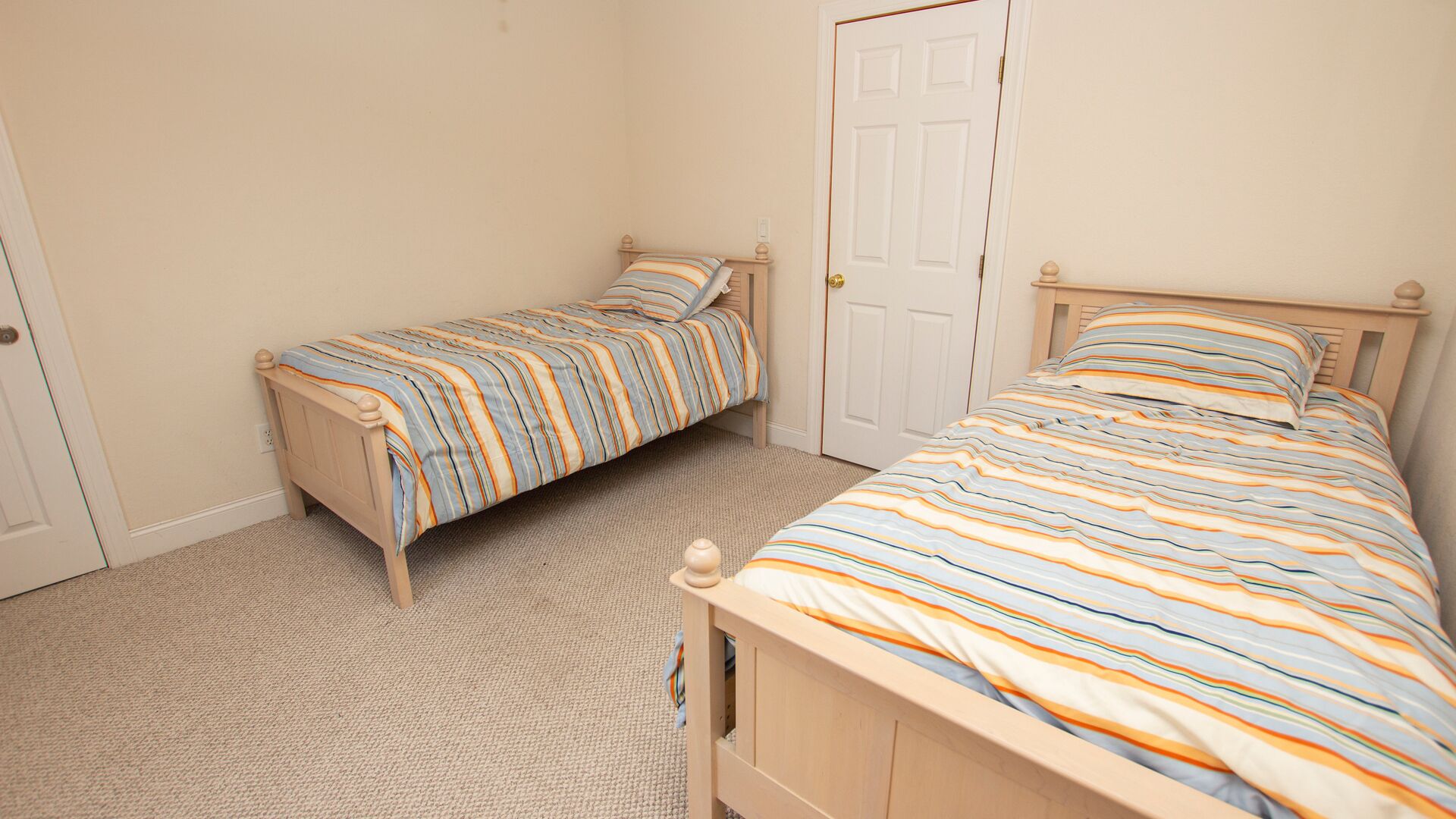 A bedroom with two single beds, a door, and a carpeted floor.