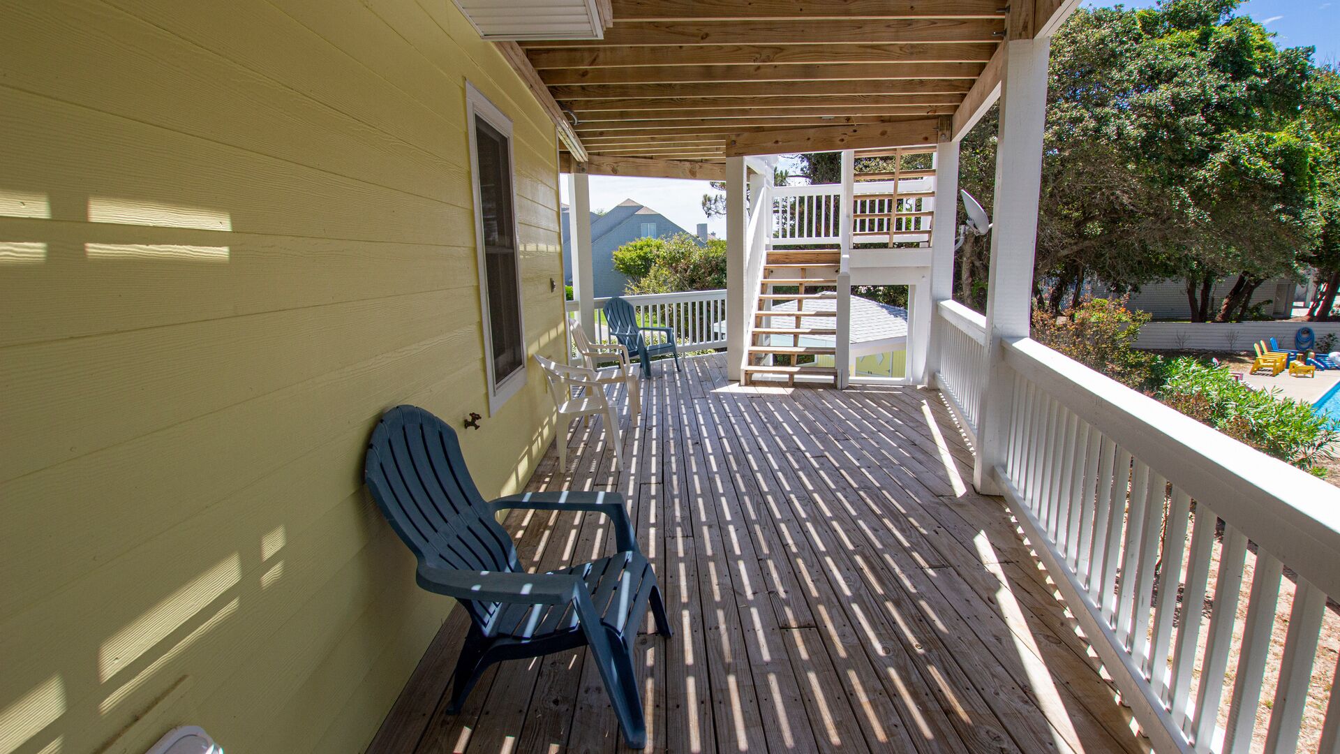 Une terrasse en bois avec une balustrade blanche, une chaise Adirondack bleue et une vue sur une montagne en arrière-plan.
