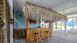 A tiki bar with a thatched roof, wooden bar counter, and two bar stools. - Bahama Breeze Canal Retreat • Dock, Fishing & Water Access • 3 Min. to Beach (Galveston)