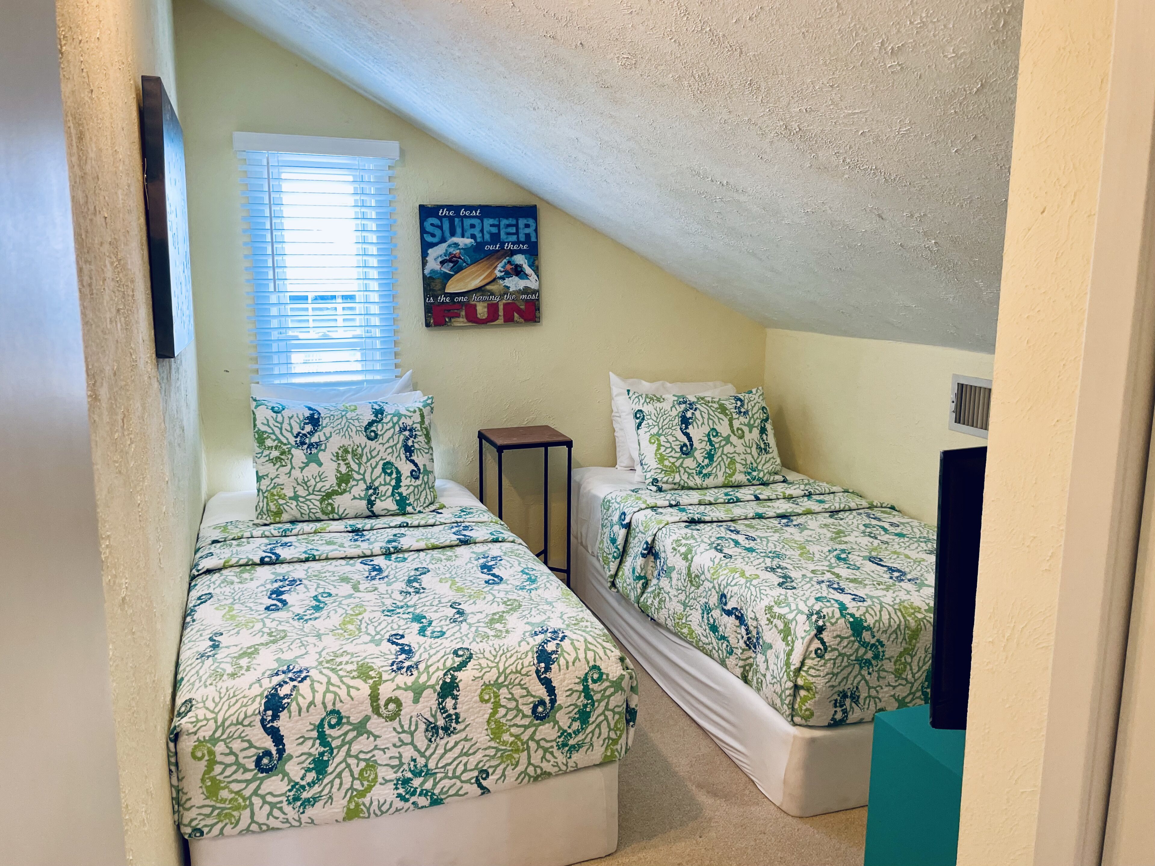 Un pequeño y acogedor dormitorio en el ático con dos camas, cada una con colcha estampada en tonos coral.