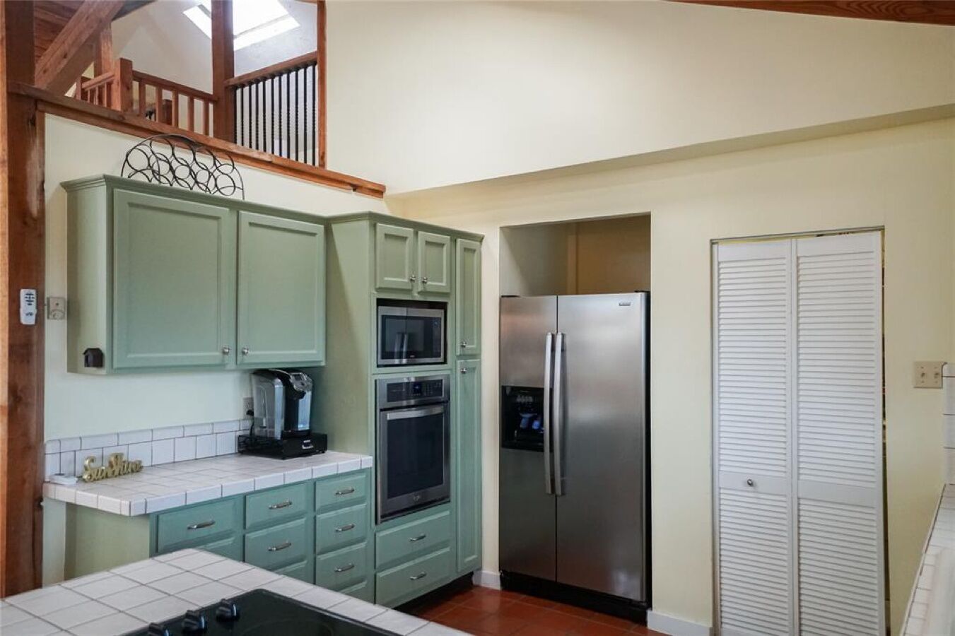 A kitchen with green cabinets, a stainless steel refrigerator, and a microwave.