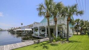 A waterfront property with a covered dock, palm trees, and a grassy area. - Bahama Breeze Canal Retreat • Dock, Fishing & Water Access • 3 Min. to Beach (Galveston)