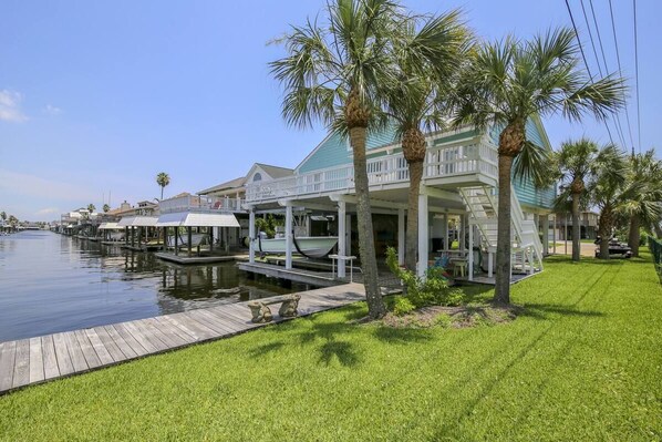 A waterfront property with a covered dock, palm trees, and a grassy area.