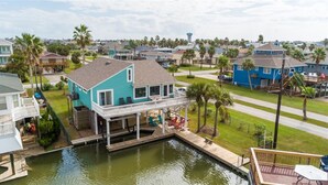 A house with a dock extending into a body of water, surrounded by palm trees and other residential buildings. - Bahama Breeze Canal Retreat • Dock, Fishing & Water Access • 3 Min. to Beach (Galveston)