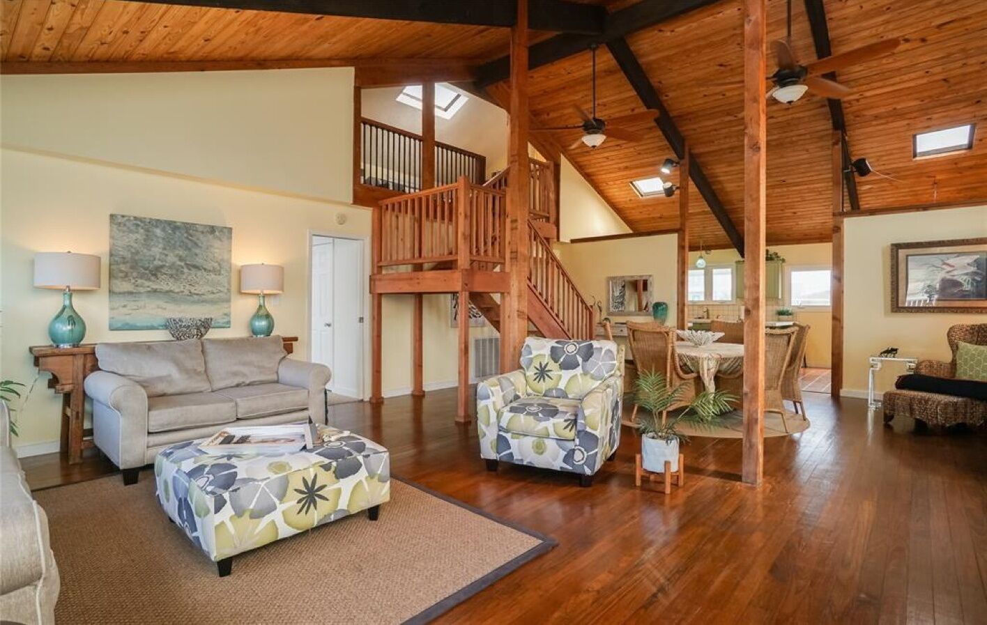 A spacious living area with a high ceiling, wooden beams, a staircase, and a dining area.