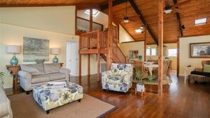 A spacious living area with a high ceiling, wooden beams, a staircase, and a dining area. - Bahama Breeze Canal Retreat • Dock, Fishing & Water Access • 3 Min. to Beach (Galveston)
