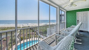 Un balcon avec vue sur la plage, une piscine et des fauteuils en osier.