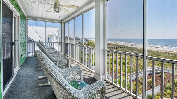 Un balcon avec des fauteuils en osier, un ventilateur de plafond et une vue sur la plage.