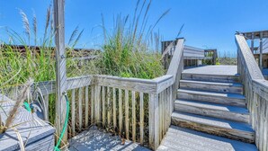 Une promenade en bois mène à une zone de plage, où se trouvent un escalier en bois et un lampadaire en métal.