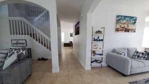 Uma sala de estar ampla com escada, um sofá cinza, uma estante de livros e um quadro de uma ponte.
