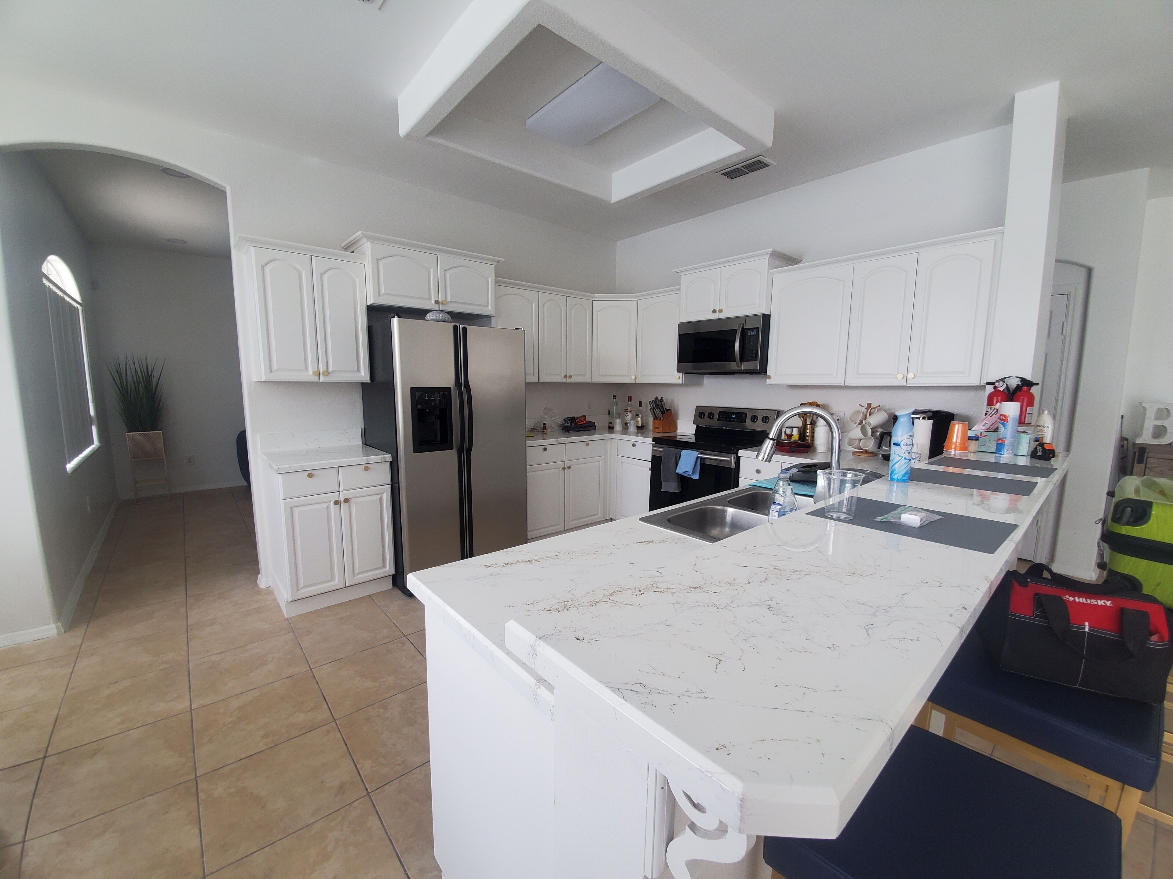 A modern kitchen with white cabinetry, a stainless steel refrigerator, a microwave, and a large island with a sink.