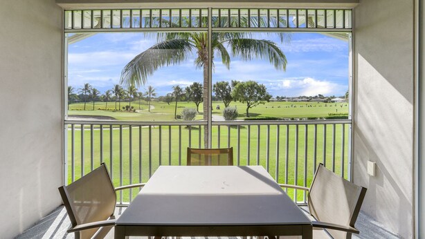 Un balcon avec une table et des chaises, donnant sur un terrain de golf bordé de palmiers et offrant une vue sur un ciel dégagé.