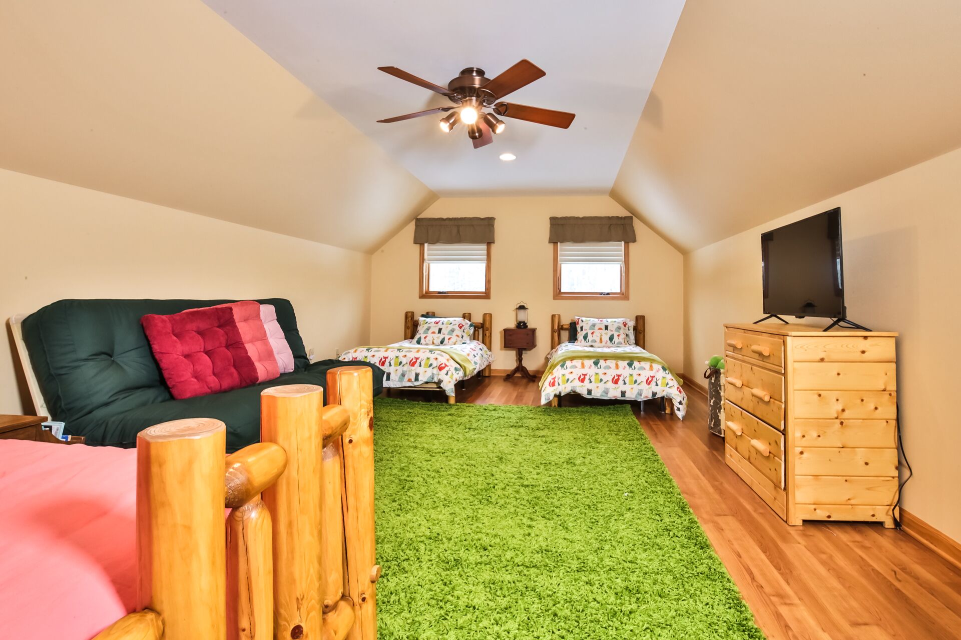 Une chambre confortable avec un canapé vert, deux lits simples, une commode en bois, un ventilateur de plafond et un téléviseur.