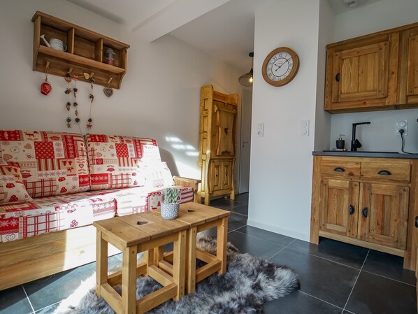 Ein gemütliches Wohnzimmer mit einem rot-weißen Sofabezug, einem Holztisch und einer rustikalen Küche mit Holzschränken und einer schwarzen Arbeitsplatte.