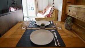 A dining table set with plates, cutlery, and glasses, with a potted plant and a wooden cabinet in the background.