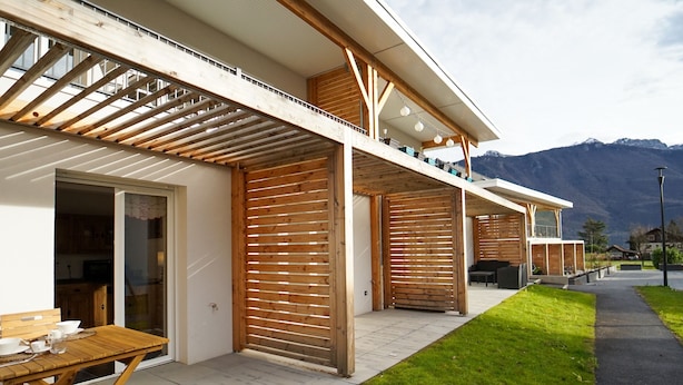A modern house with a wooden deck, a covered outdoor seating area, and a mountain view.