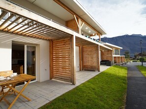 Ein modernes Haus mit einer Holzterrasse, einer überdachten Sitzgruppe und Blick auf die Berge.