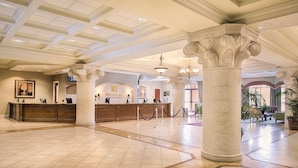 A hotel lobby with a reception desk, marble columns, and a chandelier.