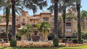 A multi-story hotel with a central fountain, surrounded by palm trees and well-maintained gardens.