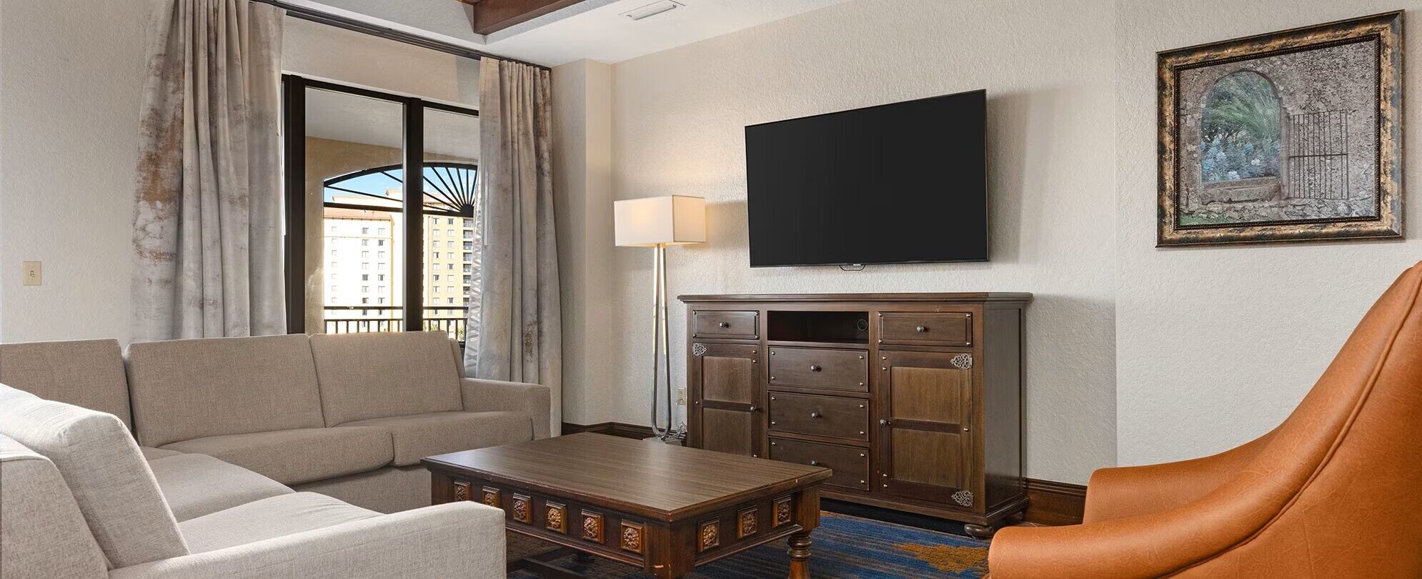 Une chambre d’hôtel avec un canapé, une table basse en bois, un meuble, un téléviseur à écran plat et un tableau encadré au mur.