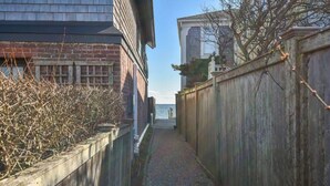 Une ruelle étroite, bordée d’une clôture en bois d’un côté et d’un bâtiment en briques de l’autre, qui mène à un quai au bord de l’eau.