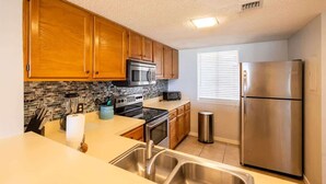 A kitchen with wooden cabinets, a stainless steel refrigerator, a microwave, and a tiled backsplash. - Turtle Dunes #1854 - Ocean Views (amelia island)