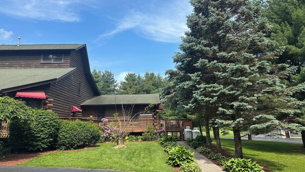 Uma cabana de toras com telhado inclinado, toldo vermelho e um deck de madeira.