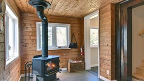 Une pièce avec un poêle à bois, des murs en bois, une fenêtre et une porte.