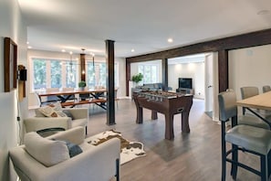 A spacious living area with a foosball table, comfortable seating, a dining area, and large windows providing natural light.