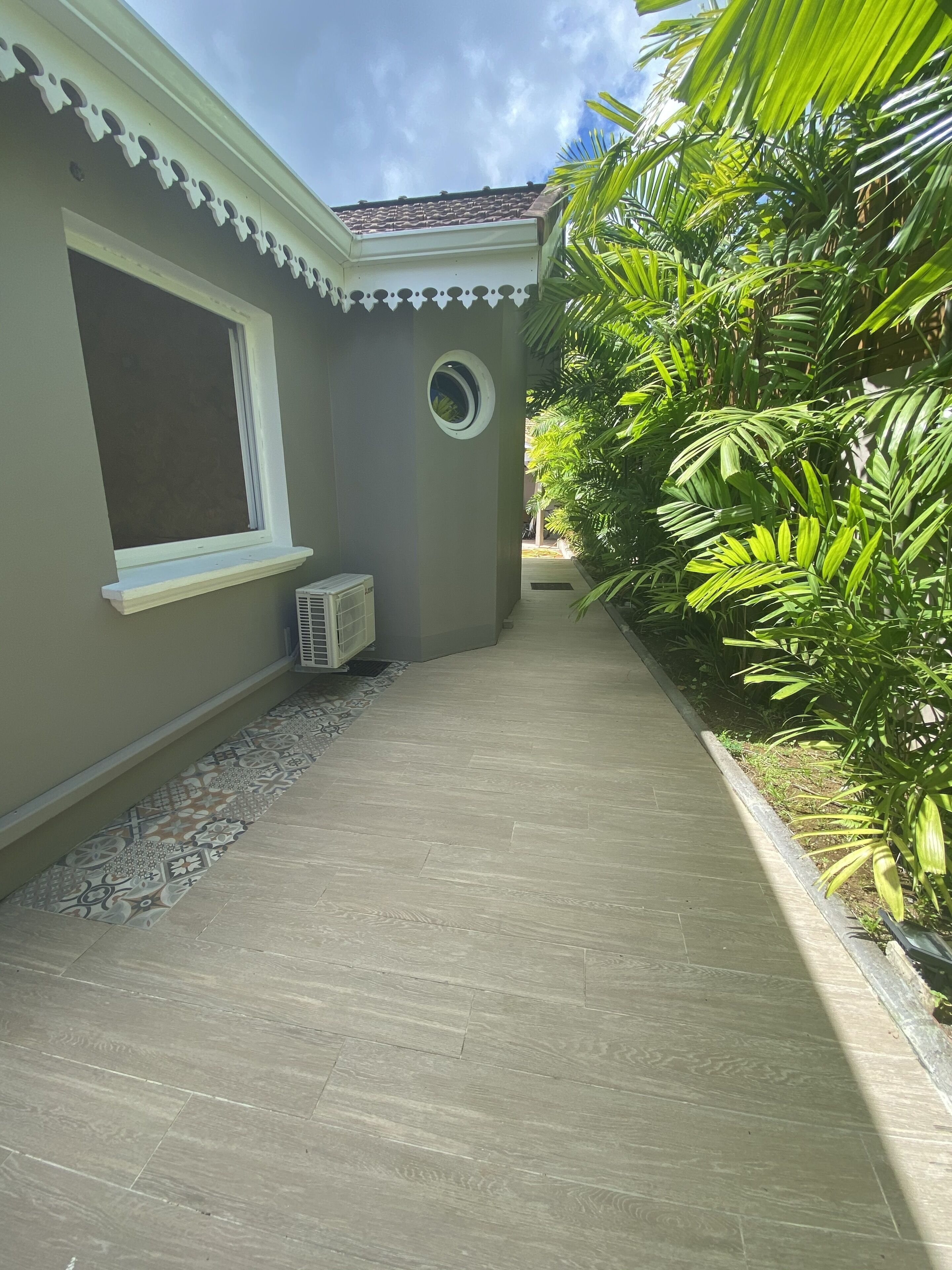 A narrow pathway leading to a building with a window and an air conditioning unit.