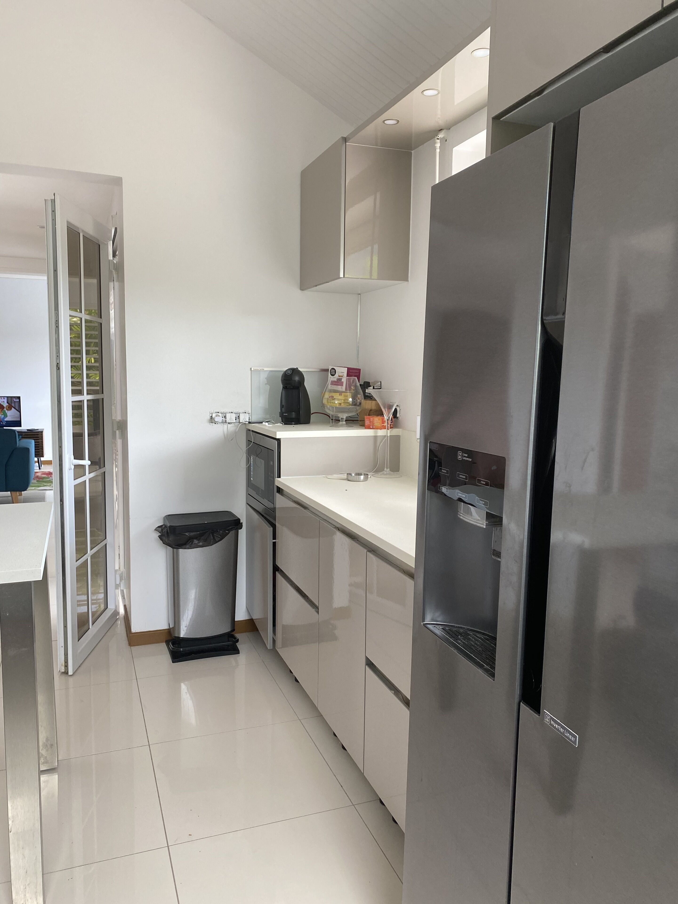 A modern kitchen with a stainless steel refrigerator, a coffee maker, and a trash bin.