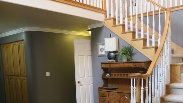A spacious living area with a wooden staircase, a dark-colored rug, and a wooden cabinet. - Fabulous Fully Furnished Vacation Home (Sandy)