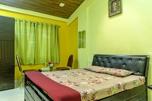 A bedroom with a bed, a chair, a small table, and a wall-mounted TV.