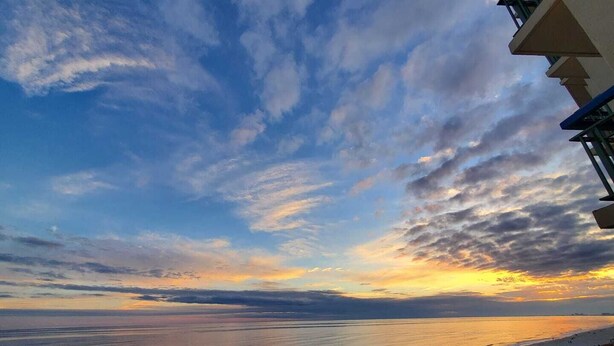 Strandudsigt med klar himmel og skyer.