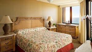 Habitación de hotel con cama, mesitas de noche, cómoda, ventilador de techo, ventana con vistas y una planta en maceta.